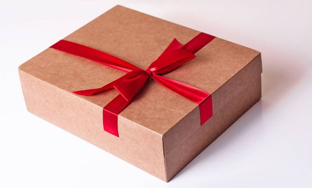 Caja de regalo marrón sobre fondo blanco.La caja está atada con una cinta roja con un lazo. - Foto, imagen