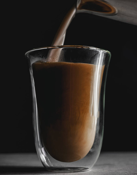 A vertical shot of milk being poured into a glass of coffee - Foto, Bild
