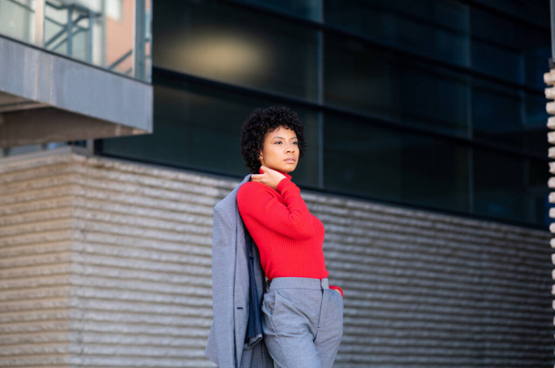 A young African-American businesswoman wearing a red turtleneck and a suit in a business building - Foto, Bild