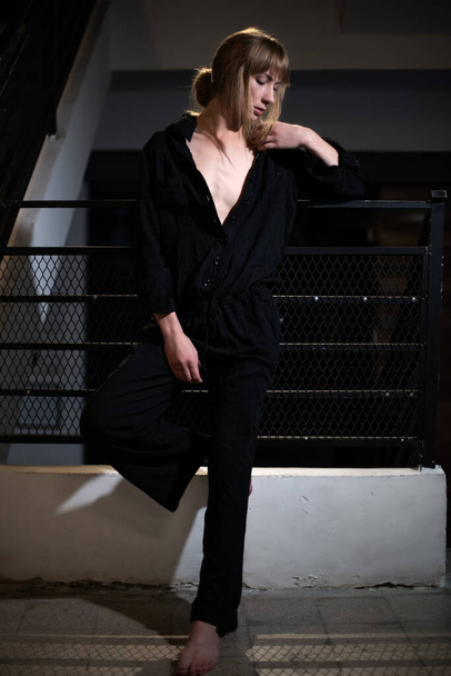 A portrait of an attractive confident Serbian woman wearing a black jumpsuit and leaning on a fence - Photo, Image