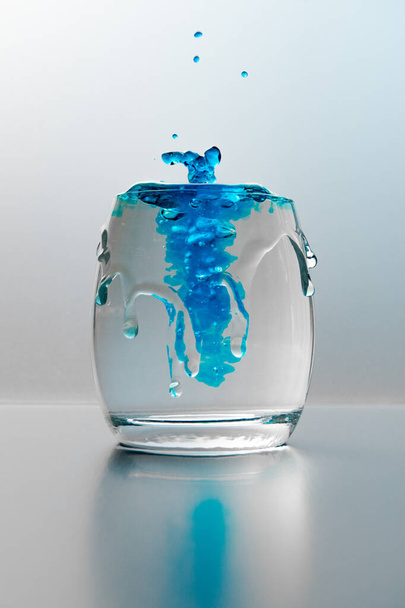 A vertical shot of a glass of water with splashes and blue paint - Фото, изображение
