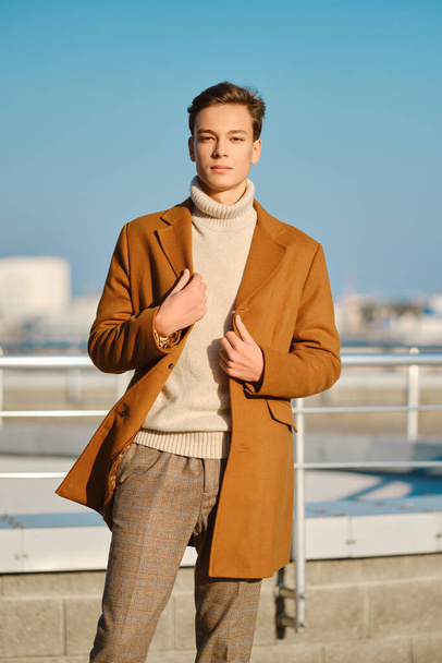 Spring - autumn outfit. Street fashion. Young man in checkered trousers, sweater wraps wool coat. - Valokuva, kuva