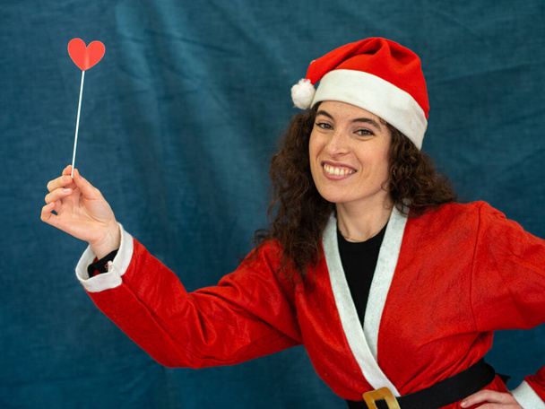 A portrait of a cheerful woman dressed up as Santa Claus holding a heart booth prop - Photo, Image