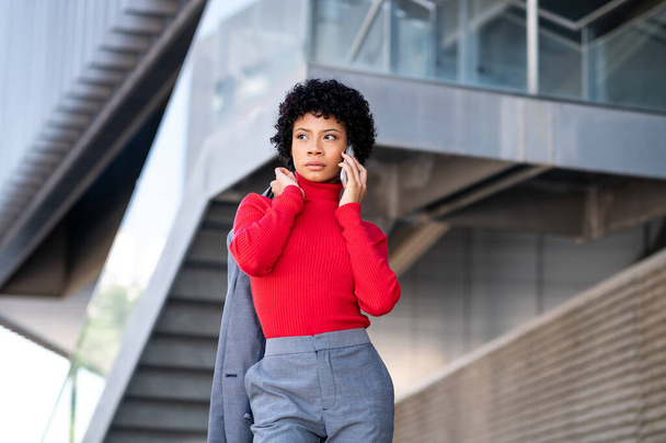 A young African-American businesswoman wearing a red turtleneck and a suit talking on a phone - Foto, Bild