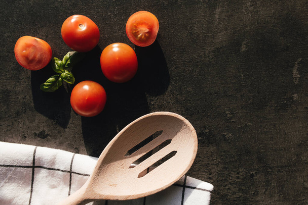 Kırmızı kiraz domatesleri, yeşil fesleğen, tahta kaşık, gri arka planda havlu. Yüksek kalite fotoğraf - Fotoğraf, Görsel
