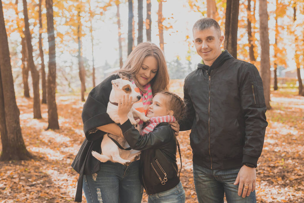 Familia pasar tiempo en el parque de otoño con un perro. Padre, madre e hija y Jack Russell terrier perro divertirse en otoño - Foto, imagen
