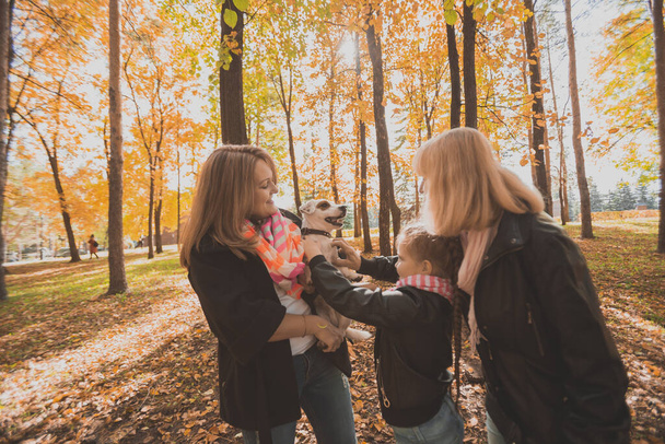 Μητέρα και γιαγιά και κόρη κατέχουν Jack Russell τεριέ και παίζει με αυτό το φθινόπωρο έξω. Έννοια κατοικίδιων ζώων και οικογένειας - Φωτογραφία, εικόνα