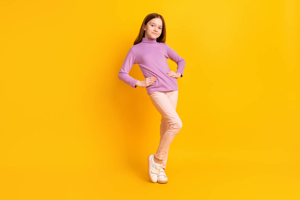 フルサイズの写真の幸せな正笑顔かなり小さな女の子身に着けているパープルセーターとピンクパンツ孤立した黄色の色の背景 - 写真・画像