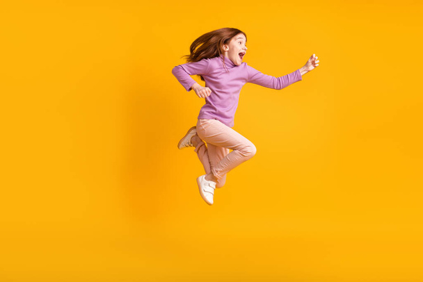Full size profile side photo of happy excited cheerful smiling little girl running in air isolated on yellow color background - Foto, immagini