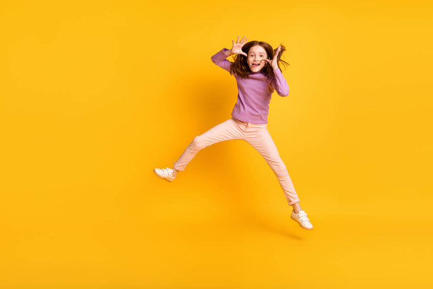 Full size photo of funky funny humorous little girl jumping fooling around showing tongue isolated on yellow color background - Fotó, kép