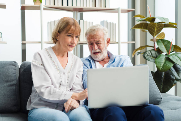 Elderly senior family couple sitting in modern living room together using laptop. Old man get confuse from modern technology. - Foto, afbeelding