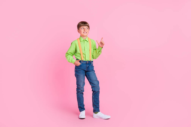 Vista completa del tamaño del cuerpo del atractivo chico alegre de moda que muestra el espacio de copia aislado sobre el fondo de color rosa brillante - Foto, imagen