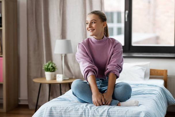 happy smiling girl sitting on bed at home - Фото, изображение