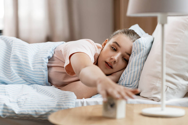 sleepy girl with alarm clock awaking in bed - Фото, изображение