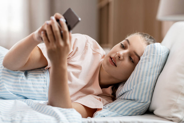 happy girl with smartphone in bed at home - Fotoğraf, Görsel