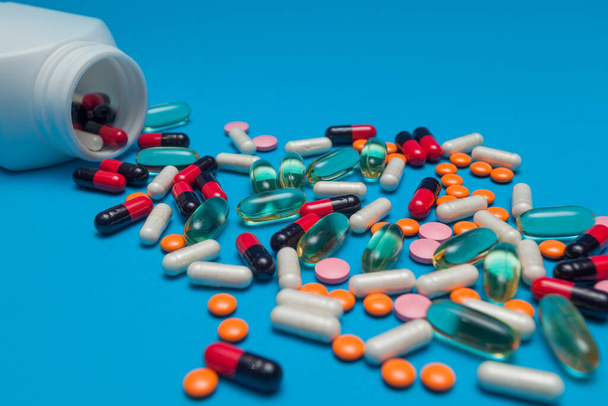 többszínű tabletták kiesnek egy tégelyből, kék alapon - Fotó, kép