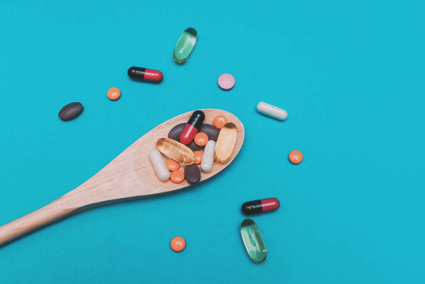 pastillas multicolores en una cuchara de madera sobre un fondo azul - Foto, Imagen