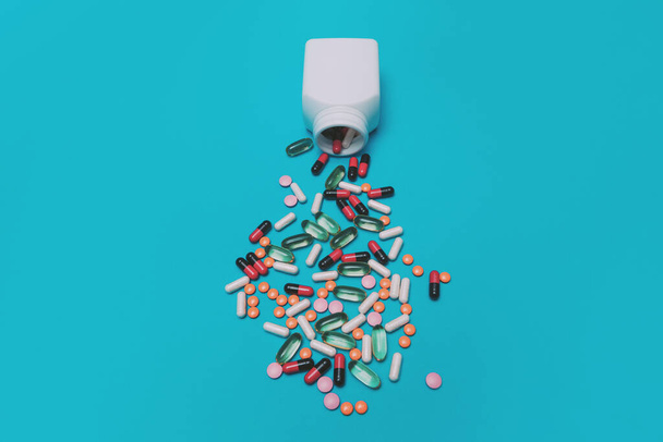 píldoras multicolores cayendo de un frasco sobre un fondo azul - Foto, imagen