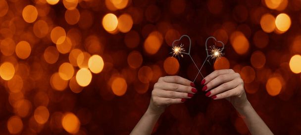 Valentýn / Láska / Svatba / Narozeniny / Silvestr / Nový rok / Party pozadí - šťastná žena drží jiskřivé srdce jiskry v rukou, s červenými nehty v noci s červenými bokeh světla - Fotografie, Obrázek