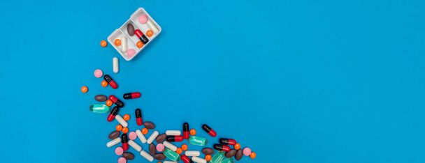 pill dispenser with multicolored pills on blue panorama background - Foto, imagen