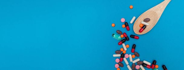 разноцветные таблетки в деревянной ложке на голубом фоне панорамы - Фото, изображение