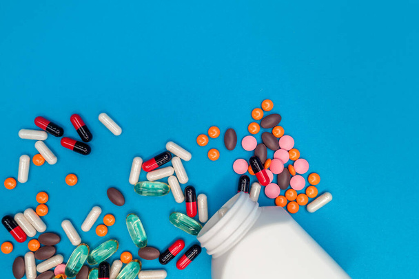veelkleurige pillen vallen uit een pot op een blauwe achtergrond - Foto, afbeelding