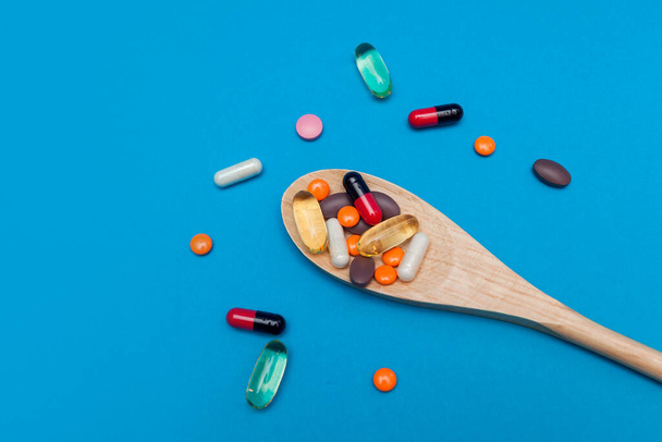 pastillas multicolores en una cuchara de madera sobre un fondo azul - Foto, imagen