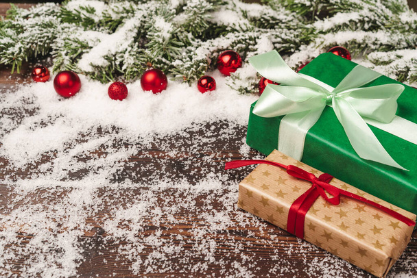 Presents on wooden background with fir tree branches and red baubles powdered with snow - Foto, Imagem