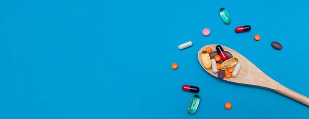 wielobarwne tabletki w drewnianej łyżce na niebieskim tle panoramy - Zdjęcie, obraz