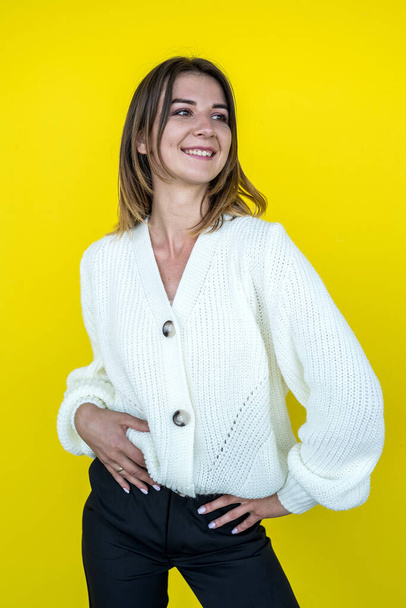 fashion portrait of a young pretty girl posing for the camera dressed in a knitted white sweater in front of a yellow wall - Foto, Imagem