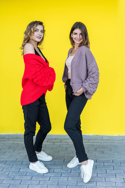 Divat barátnők viselnek modern kötött pulóver pózol sárga fal, mint a háttér. - Fotó, kép