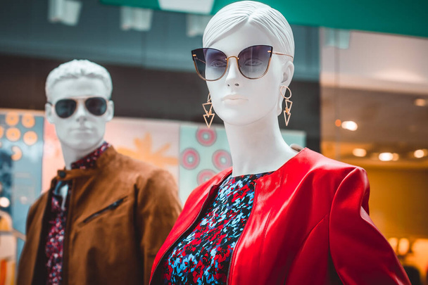Lengyelország, BYDGOSZCZ - 2019. november 23.: Női és férfi próbababák. Fényes portré női báburól napszemüvegben és piros kabátban a kirakatban lévő próbababás férfi hátterével szemben. Családi vásárlás - Fotó, kép