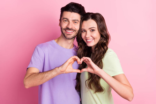 Portrait of attractive amorous cheerful couple embracing showing heart symbol isolated over pink pastel color background. - Foto, afbeelding