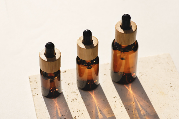 Янтарные стеклянные бутылки с бамбуковой крышкой на каменной пластине. Средства для ухода за кожей, натуральная косметика - Фото, изображение