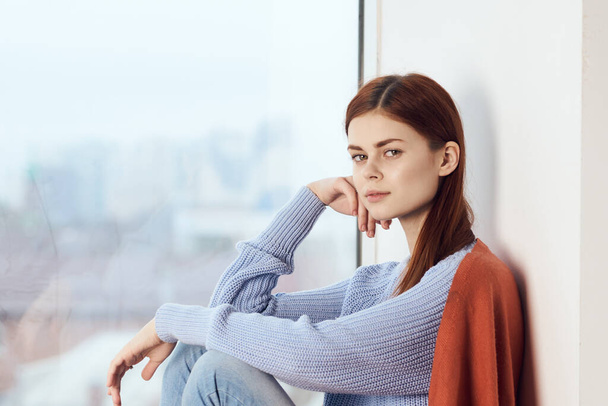 woman with sad expression sits by the window with a plaid - Zdjęcie, obraz