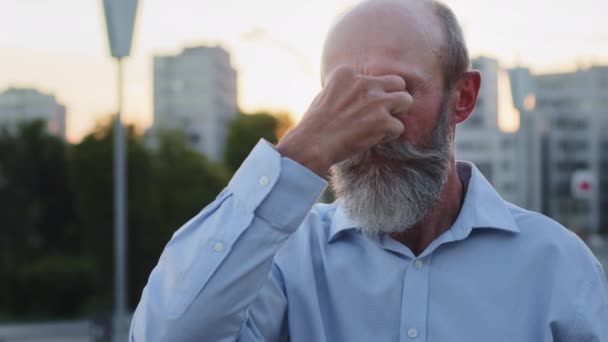 Fejlövés közelkép fáradt középkorú férfi szürke szakállal és bajusz dörzsölés orr híd a szabadban. Frusztrált stresszes idős nagyapa szenved homályos látás, szemfeszülés - Felvétel, videó