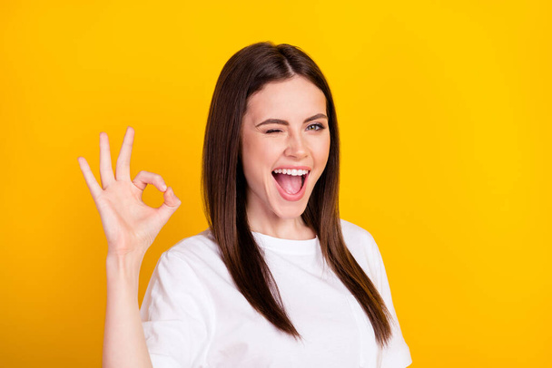 Photo of happy funky funny smiling cheerful girl wink blink eye showing okay sign isolated on yellow color background. - Fotografie, Obrázek