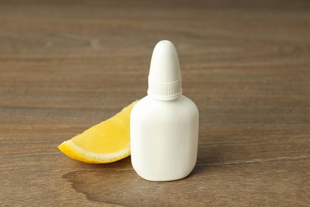 Prázdná láhev nosní sprej a citron plátek na dřevěném pozadí - Fotografie, Obrázek