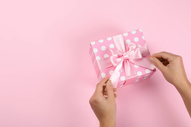 Female hands and gift box with bow on pink background - Photo, Image