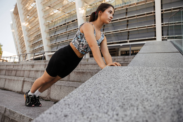 Adolescente chica entra para los deportes y hace flexiones desde el suelo en el fondo de la ciudad - Foto, Imagen