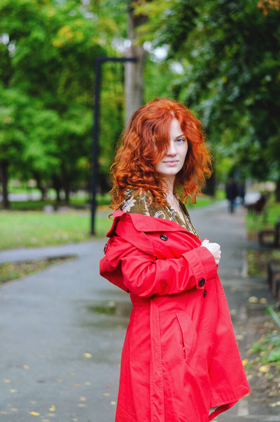 Молода щаслива жінка з рудим волоссям, веснянки, блакитні очі в червоному береті, пальто, що йде в осінньому парку, посміхається. Жовте осіннє листя
. - Фото, зображення