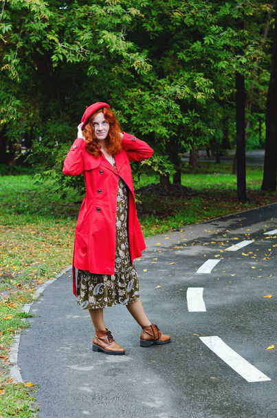 Young happy woman with red hair, freckles, blue eyes in a red beret, coat walking in autumn park, smiling. Yellow fall leaves. - Фото, изображение