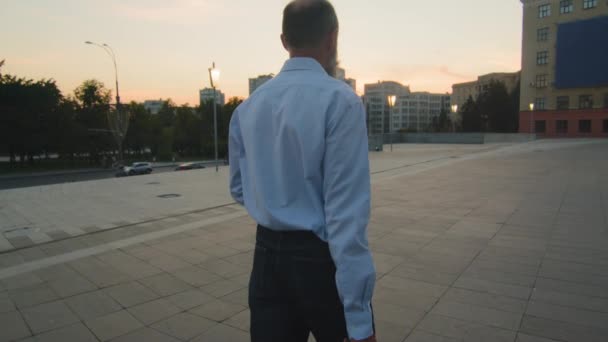 Back view of elderly tired caucasian man in white shirt with business briefcase returning in evening after hard day at work. Male pensioner, retirement age person walking at sunset outdoors in city - Filmagem, Vídeo