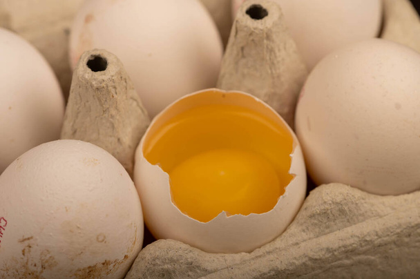 Witte kippeneieren en een gebroken ei in een dienblad van wit karton, close-up selectieve focus - Foto, afbeelding