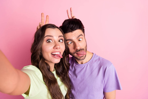 Self-portrait of beautiful friends friendship trendy crazy couple hugging showing v-sign horn grimacing isolated over pink pastel color background - Foto, afbeelding