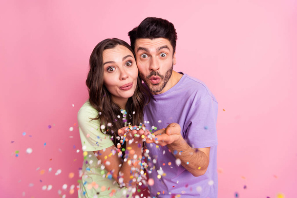 Portrait of attractive funny cheery couple embracing blowing decoration festal mood isolated over pink pastel color background - Zdjęcie, obraz