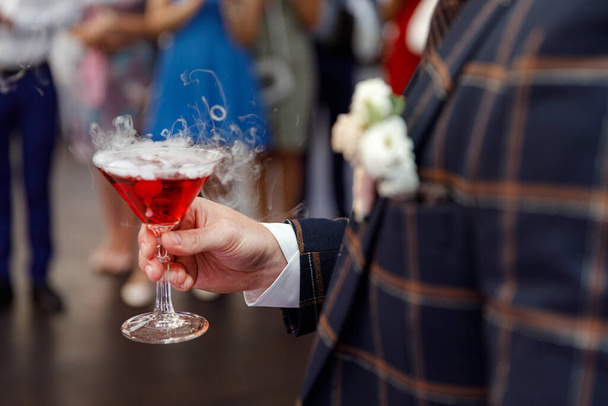 Glas champagne met droog ijs in de hand van de bruidegom - Foto, afbeelding