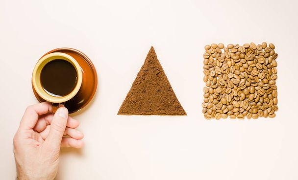 Mans hand holds black coffee, in a brown ceramic cup in vintage Scandinavian style. Circle, square, triangle. Roasted and ground coffee beans. Concept. - Fotografie, Obrázek
