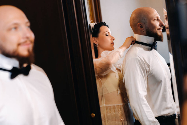 The bride in boudoir underwear dresses the groom in the interior of the hotel. - Photo, image