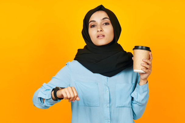 vrouw in zwart hijab met klok in handen technologie emoties geel achtergrond - Foto, afbeelding